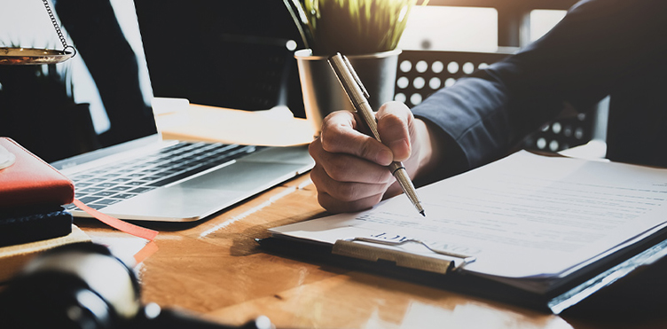 Photo of an individual at a desk with a laptop and writing in a notebook