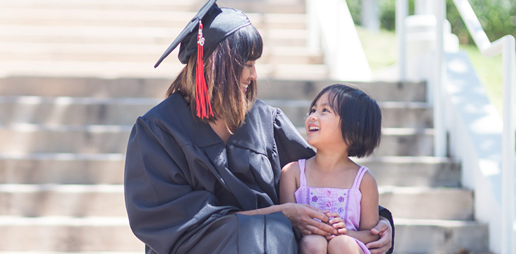 Mother and child sitting on the steps with the mother in a graduation cap and gown