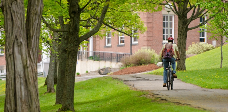 A student bikes along a sidewalk on a UNB campus